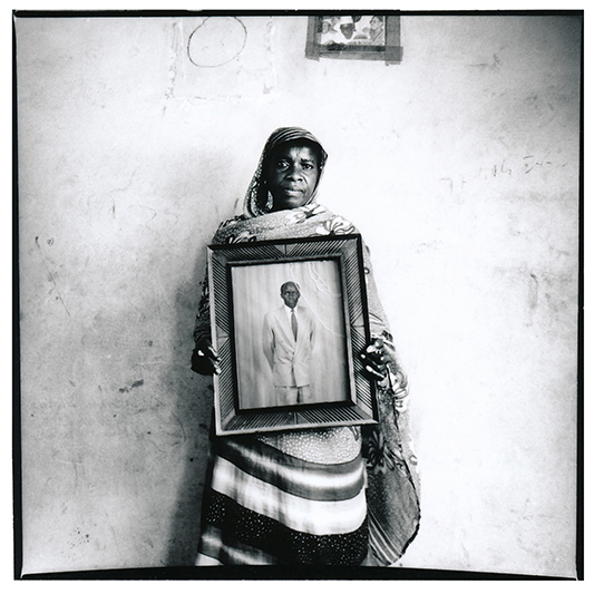 A Louga, Ndeye Ba fut l'une des seules épouses d'émigrés à m'autoriser à la photographier à visage découvert. Sans nouvelle de son homme depuis presque deux decennies, elle parait encore abasourdie par cette attente qu'elle refuse de transformer en deuil. Elle n'est ni divorcée, ni veuve. Elle n'a jamais pu se remarier. Elle montre un portrait de son mari, en Belgique la dernière fois qu'elle l'a eu au téléphone, il y a plus de 15 ans. Elle est toujours à sa recherche :